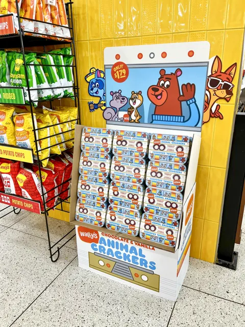 A photo of a cardboard display of animal crackers inside a store, next to a rack of chips. The display has a number of cartoon animals on it looking at the viewer.