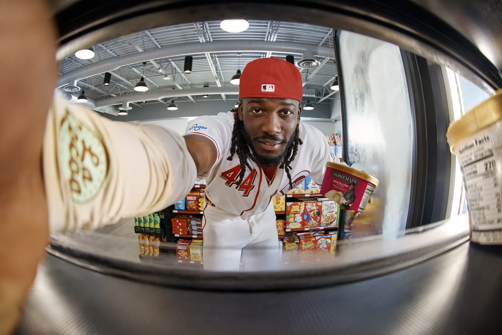 A photo of a person holding a container of ice cream in one hand and taking a fish-eye photo with the other. The person is standing inside a store.