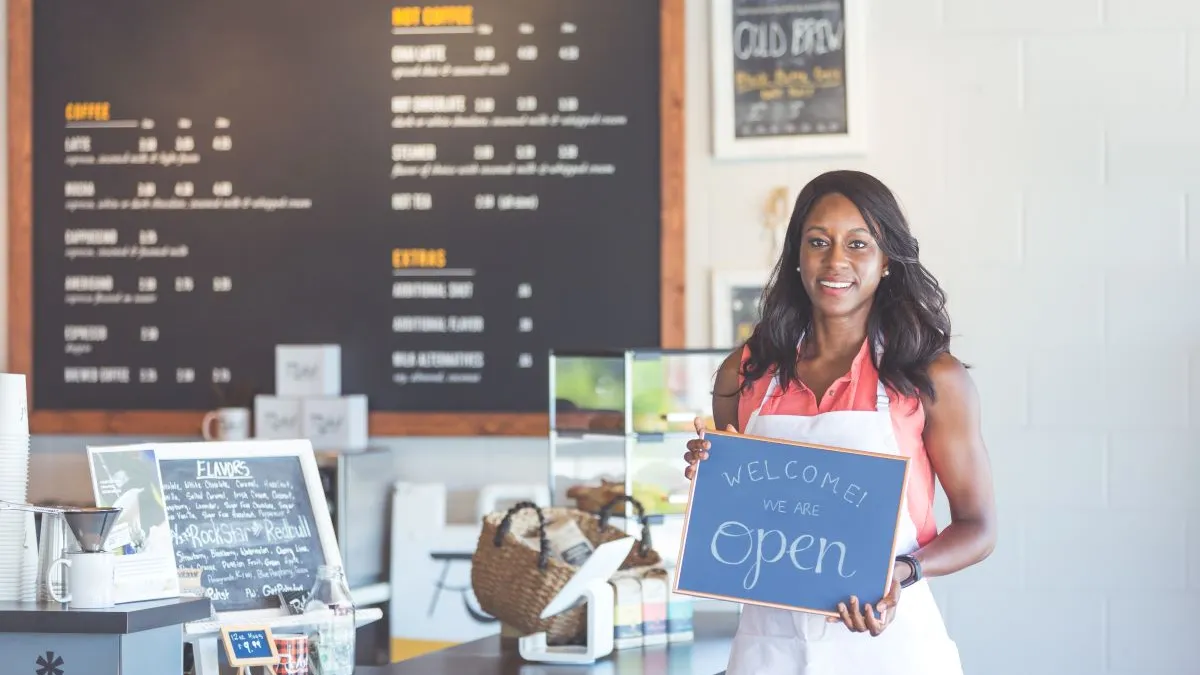 A photograph of a cafe operator holding up an open sign.