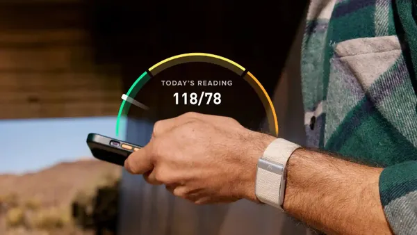 A close up of a person's wrist with a white strap around it. They're holding a phone with a displayed blood pressure reading.