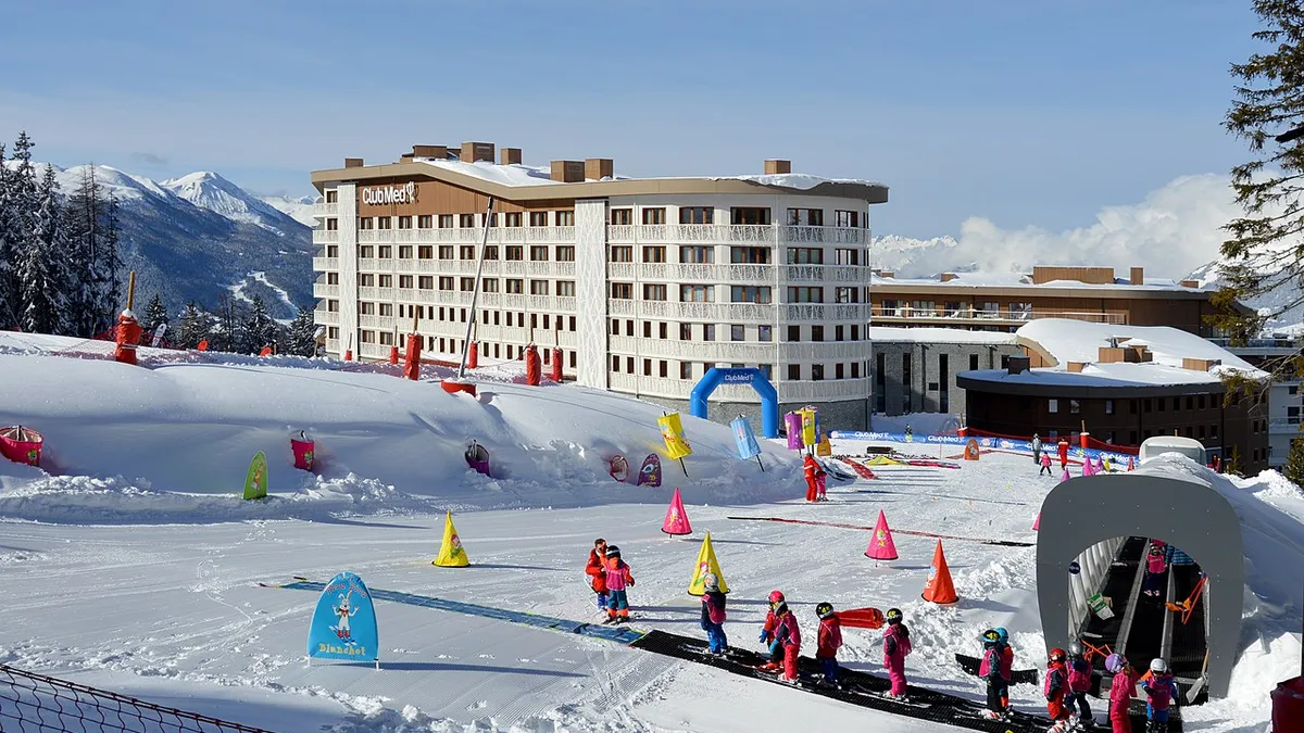 Skiers in line in the snow in front a Club Med resort