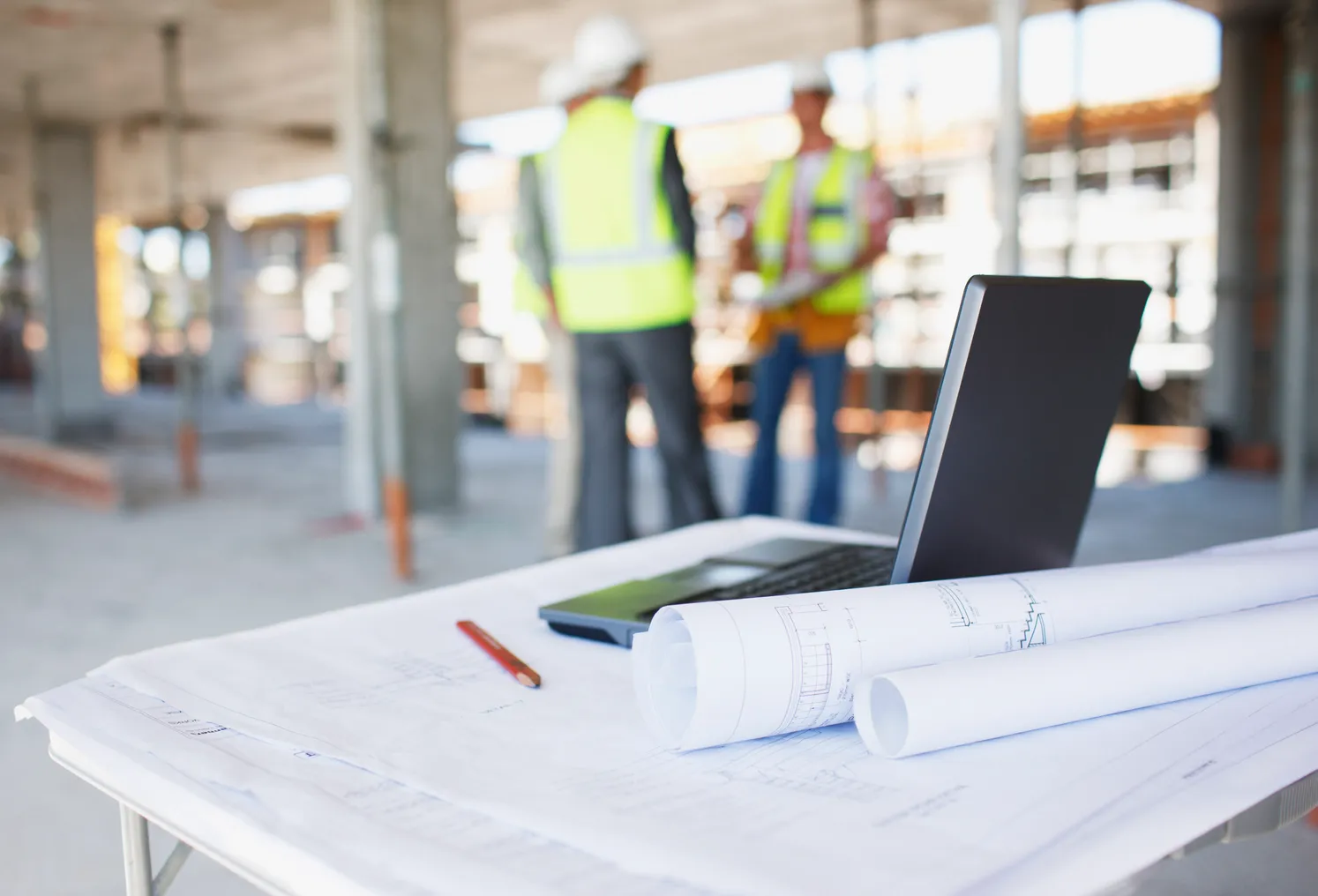 Construction workers in the background, while a laptop and office supplies are in the foreground.