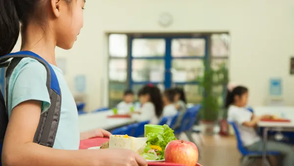 A young female student is holding a food tray in the school cafeteria.