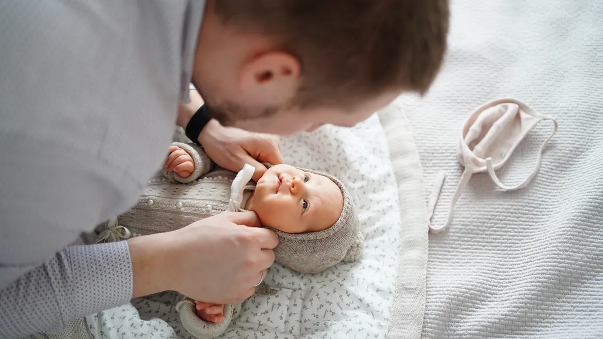 The camera points down on a man as he faces and dresses his baby on the floor.