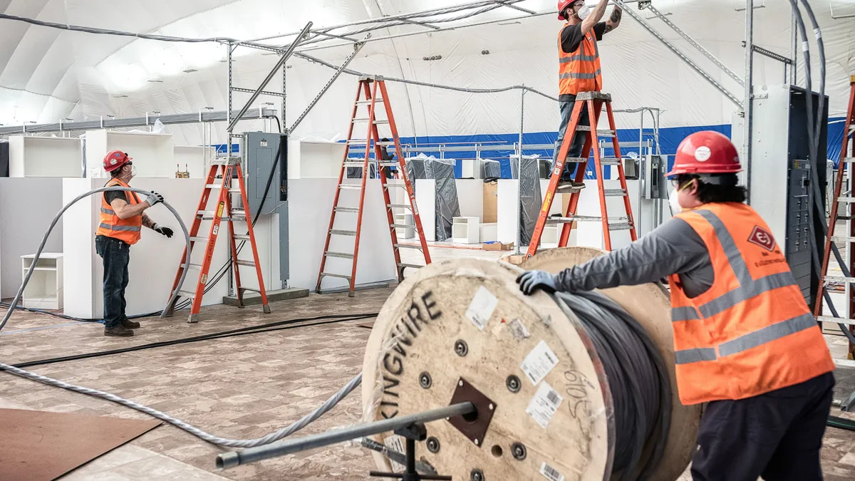 Construction workers build a structure while wearing masks.