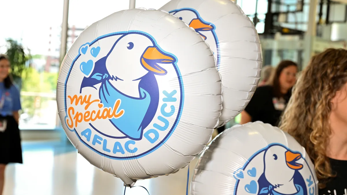 A woman holds balloons featuring the Aflac duck.