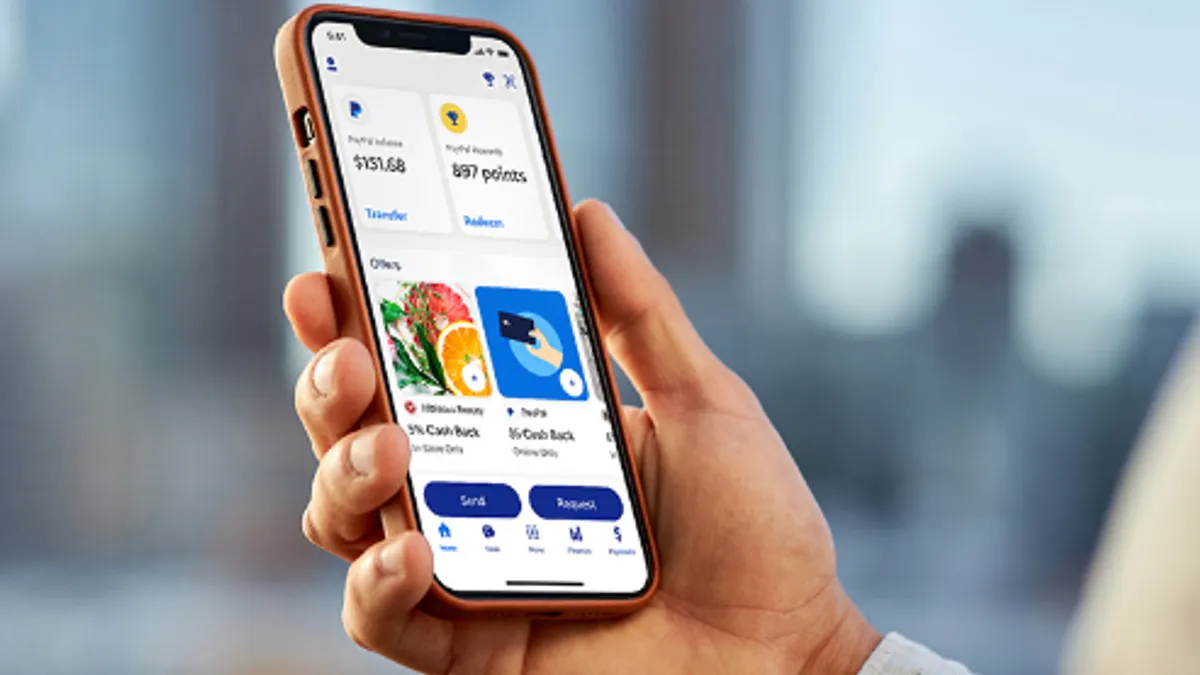 A hand holds a mobile phone with the PayPal app pulled up.