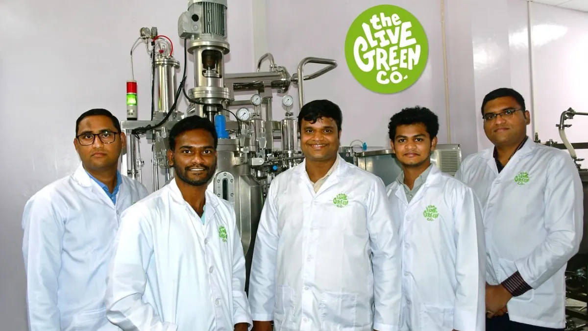 A group of people in lab coats stand in front of a lab with tanks for precision fermentation behind them.