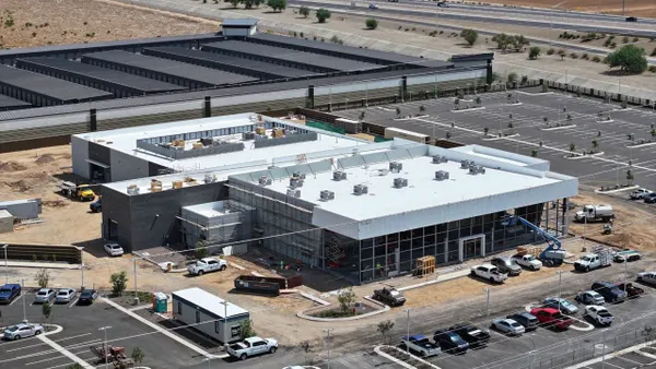 An aerial view of a building on a desert-like type of ground, with cars in a parking lot surrounding the sleek and shiny structure.