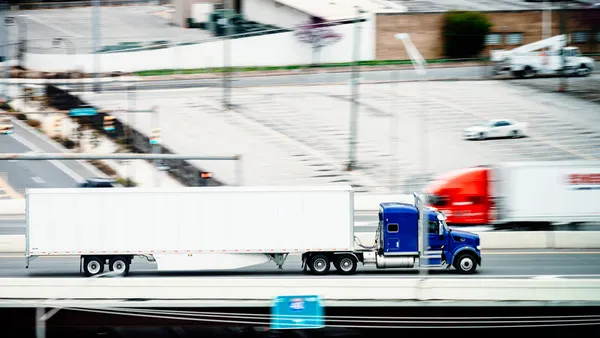 A blurred photo captures the speed of two trucks going opposite ways on a highway with a parking lot in the background.