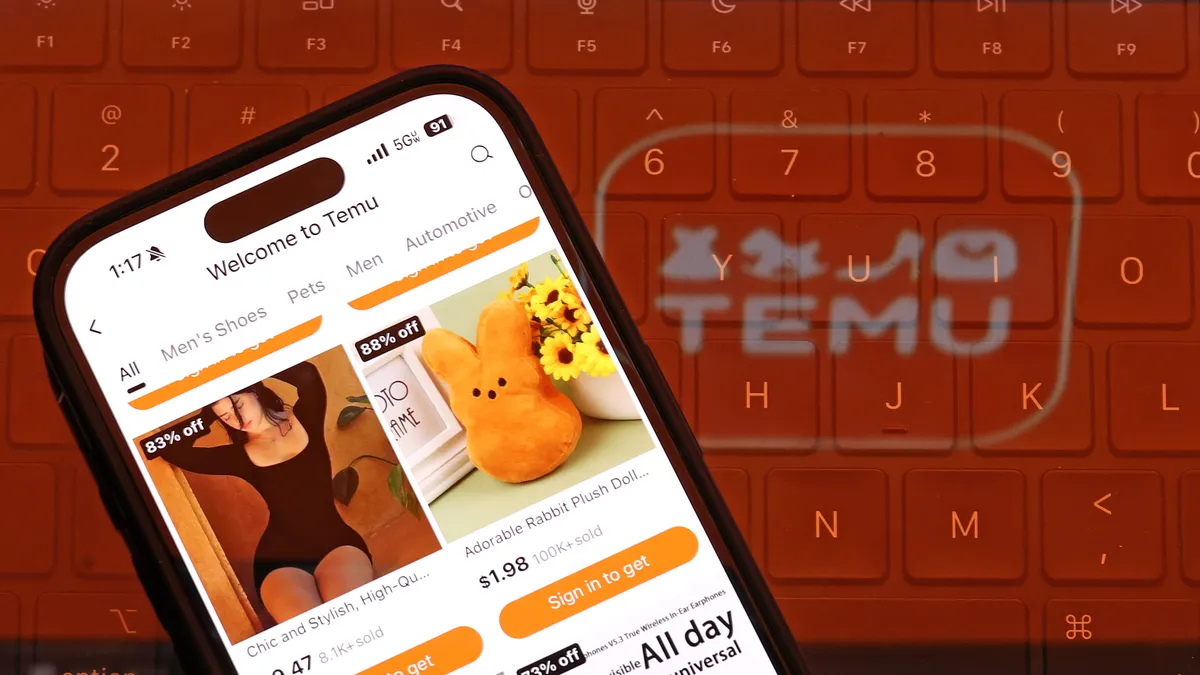 A laptop keyboard is illuminated in orange by the Temu logo. A cell phone is in front of it, with the Temu app on display.