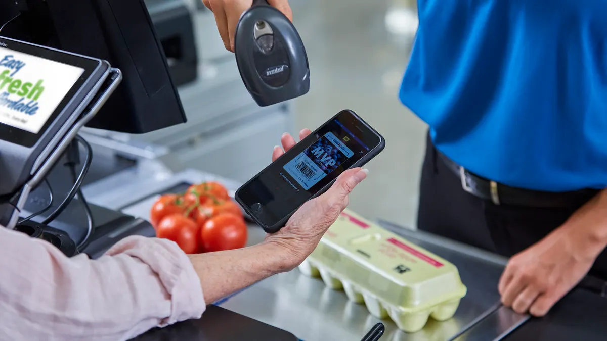 A grocery shopper getting their loyalty program barcode scanned at checkout.