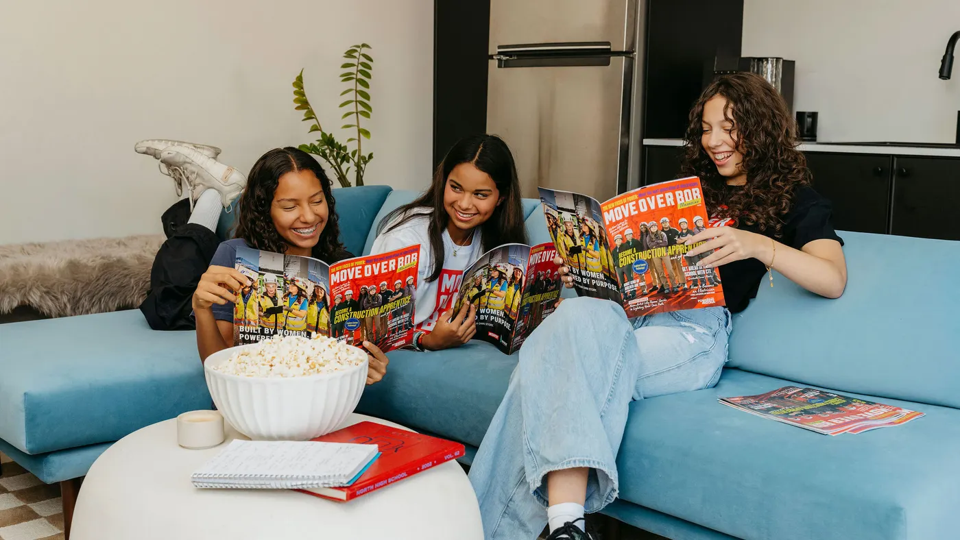 Three girls read a magazine on a couch.