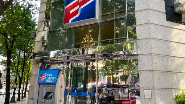 The "First Citizens" logo is shown above a doorway on a stone building with mirror panels. An ATM with the words "First Citizens Bank" sits next to the door.