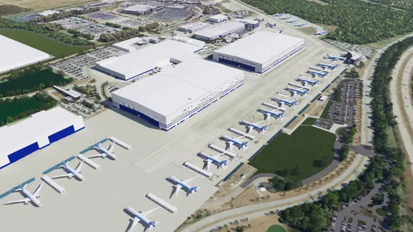Four industrial buildings in the center with a row of airplanes in front of them.