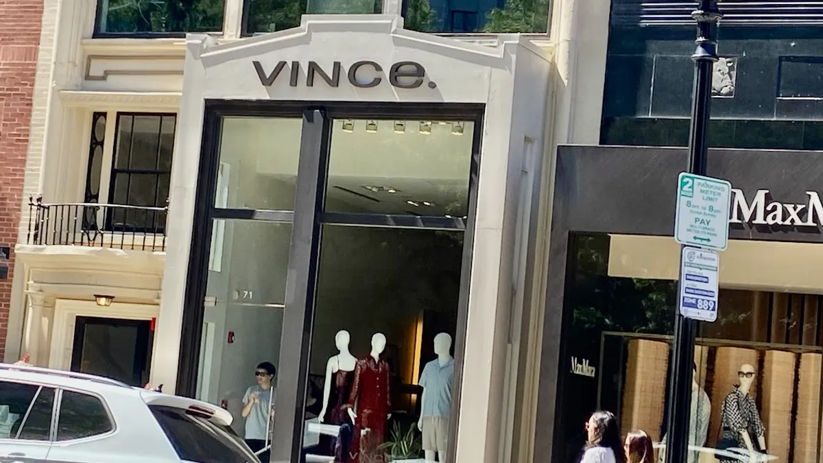 A person and mannequins stand inside a store, seen through the store window.