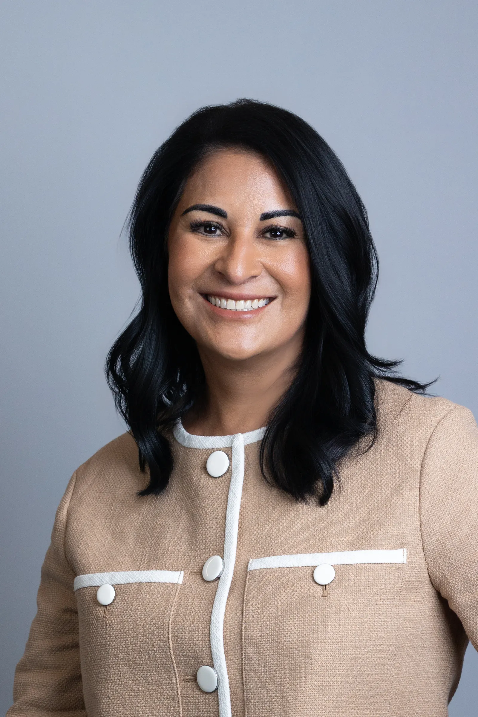 A person smiles for a portrait while wearing a beige and white jacket.