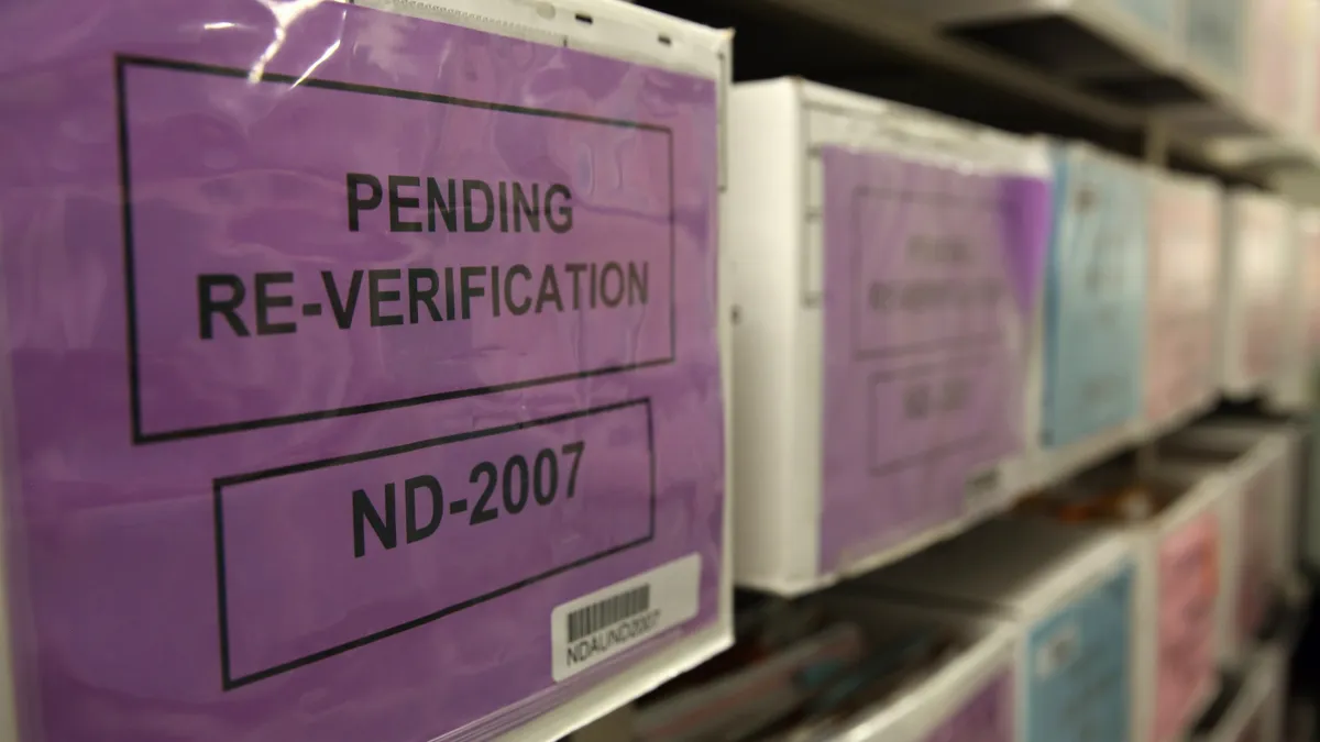 Rows of boxes sit on a shelf. The closest one bears a sign that reads "pending re-verification."