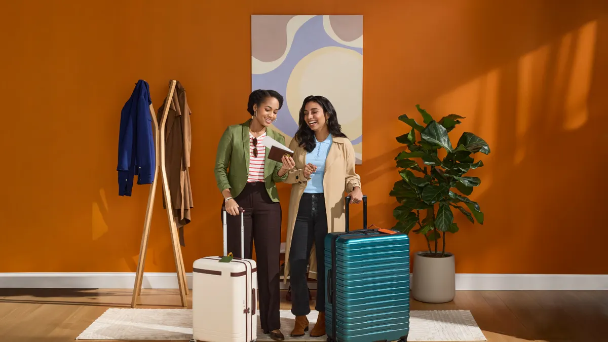 Two women standing in front of a wall with luggage by side