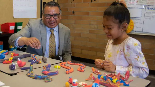 An adult and a young students are sitting at a table. In front of them are figures created with  Play-doh