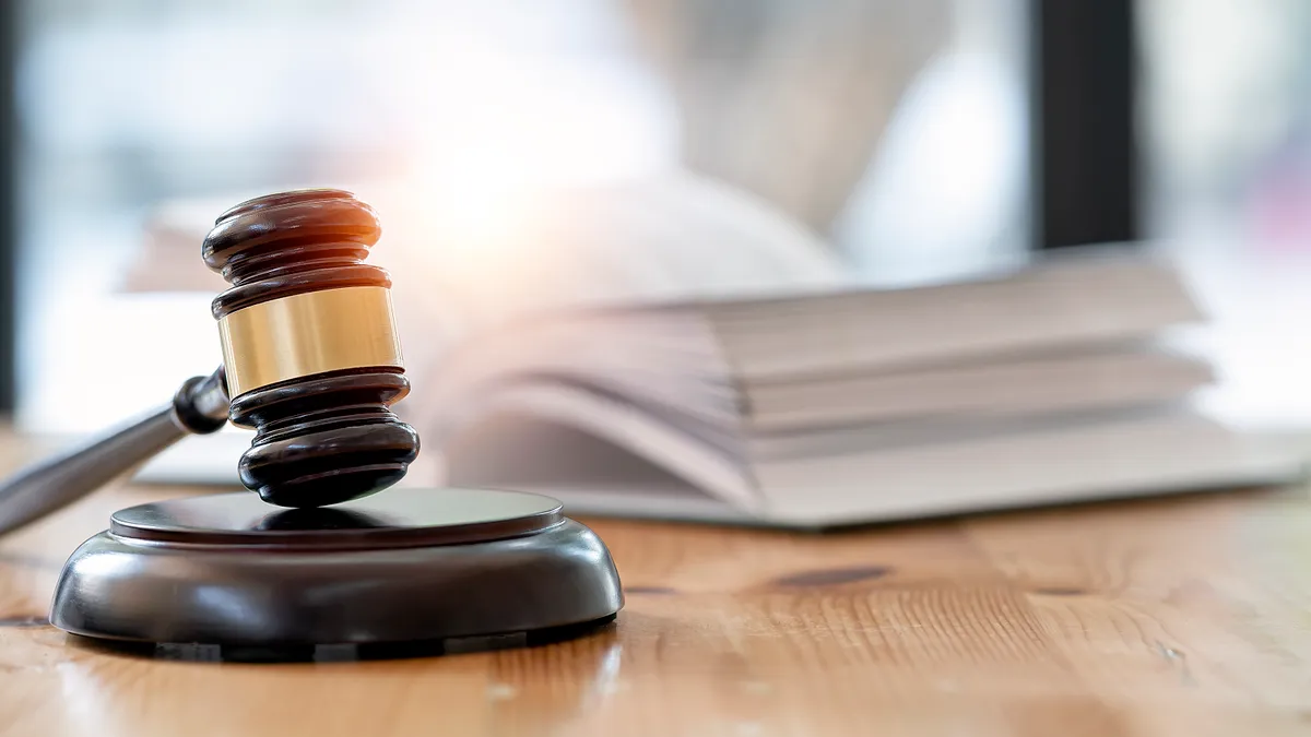 Wooden brown judge gavel on the table, with an book opened and blurred in the background.