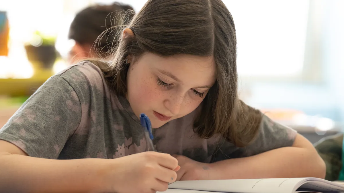 A student at a school desk looking down working in workbook