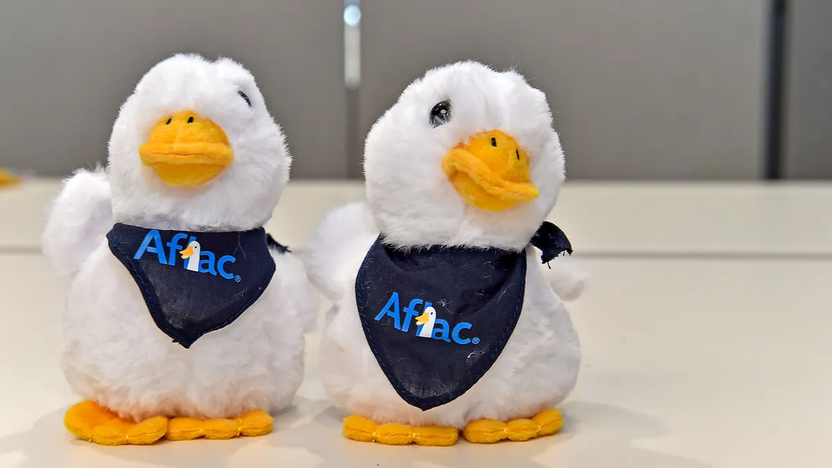 Two stuffed ducks wearing Aflac-logo bandanas appear on a table.