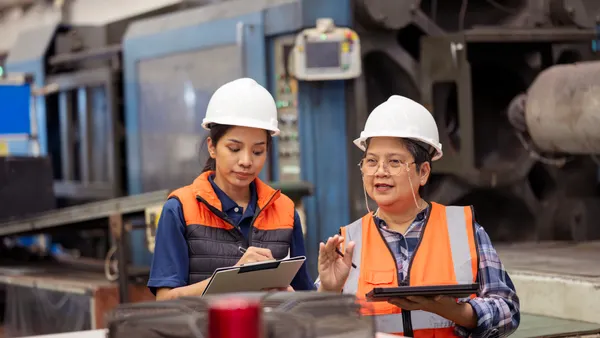 Predictive Maintenance Increase Manufacturing Productivity and Efficiency. Senior Plant Manager discussing maintenance plan with female maintenance engineer in front of machinery at factory shop-floor.