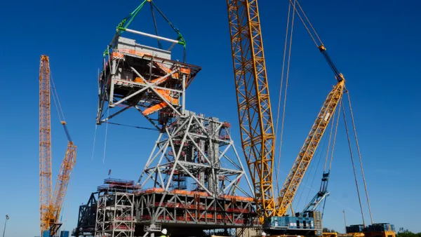 A crane lifts a heavy piece of metal onto another structure in a brightly lit day.