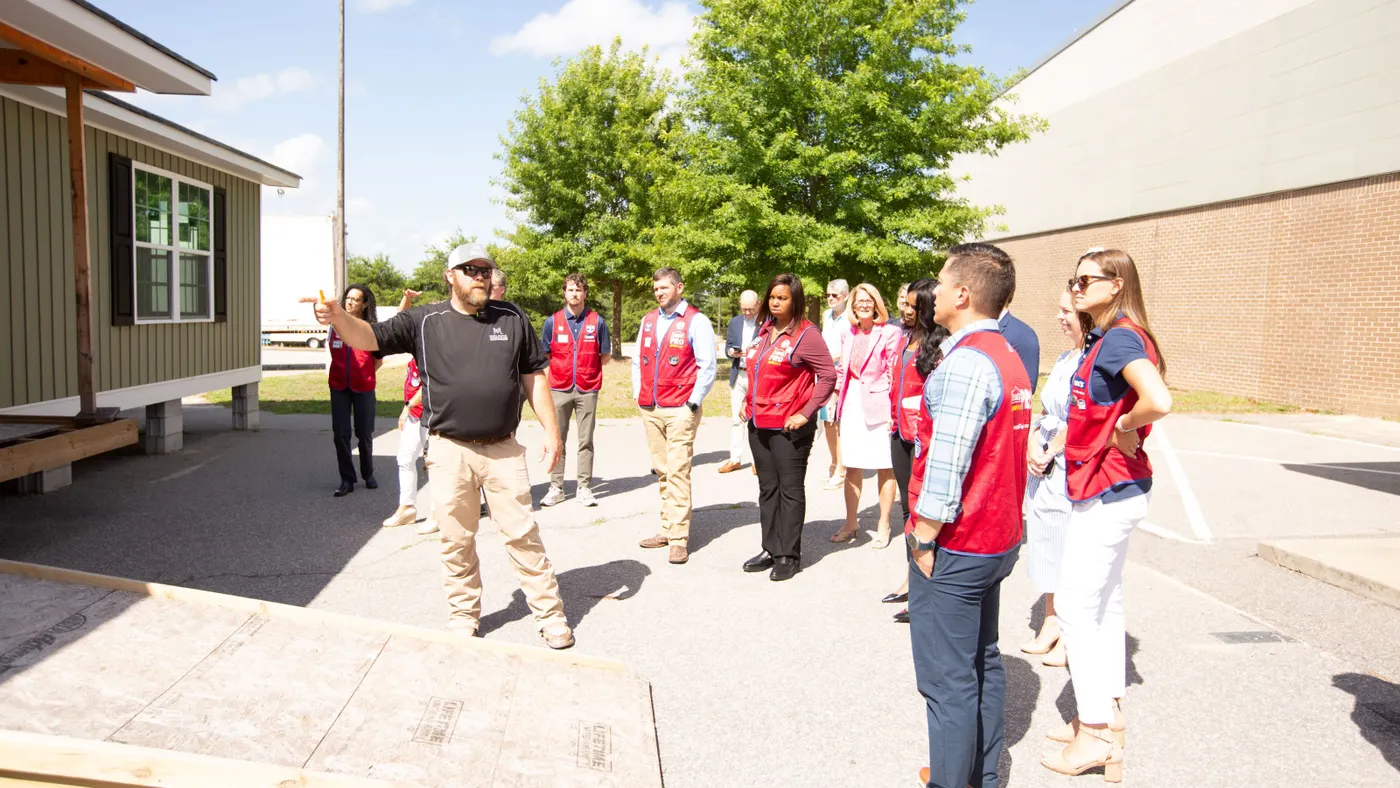 A group of people stand near a prefabricated house project.