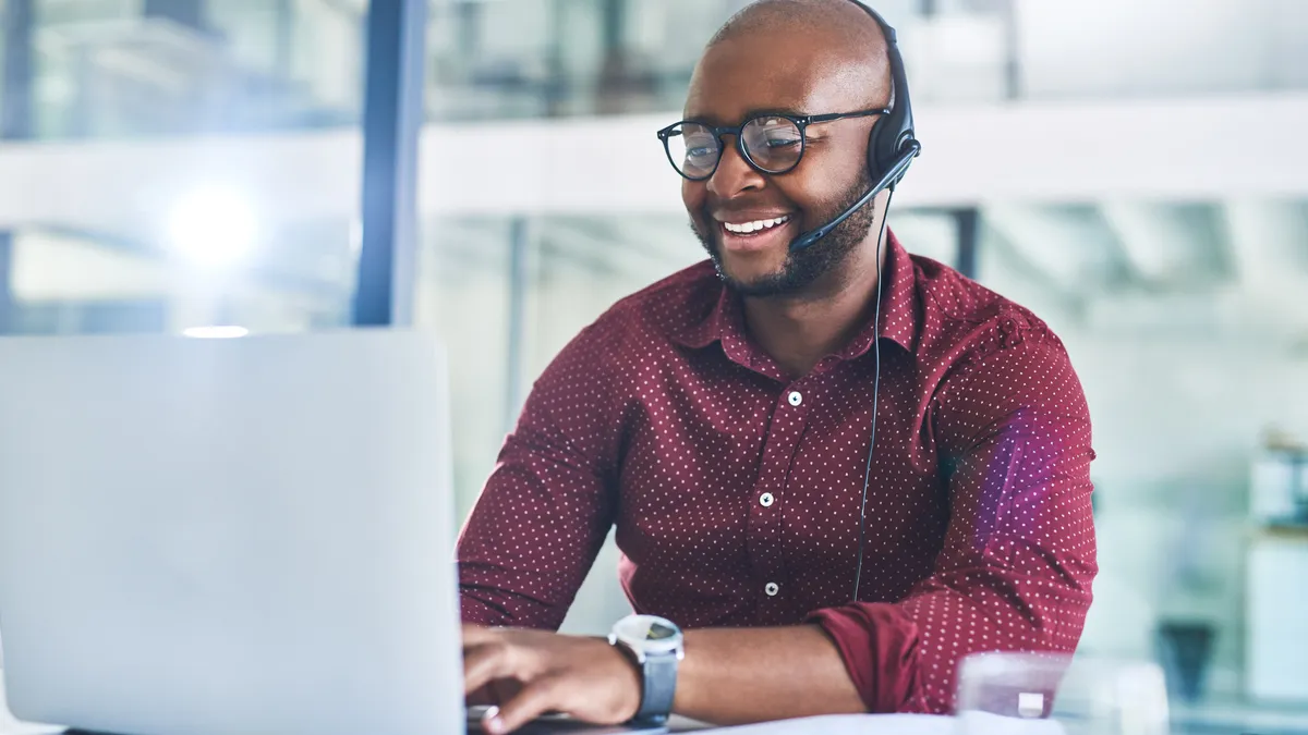 Cropped shot of a person working on a laptop with a headset