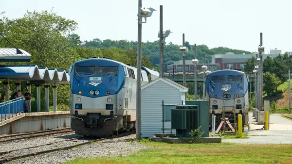 Two locomotive lable Amtrak next to a station platform with people on it.