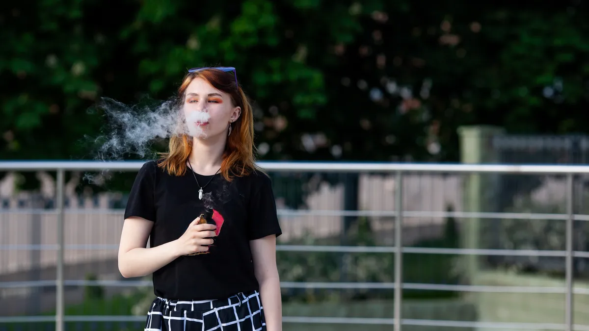 A teenager smokes from an e-cigarette outdoors.