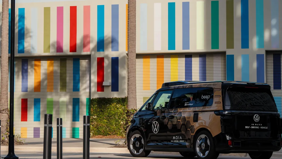 A Volkswagen van lettered for "Beep" and "Moia" parked in front of a multicolor windowless building.