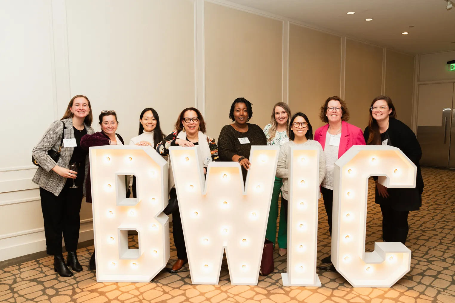 A group of women pose behind a sign reading BWIC.