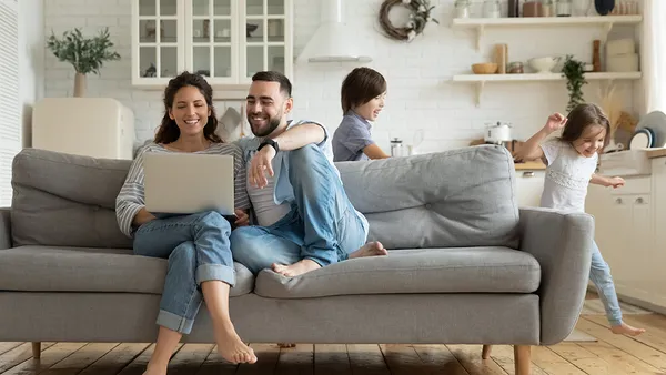 While active kids running parents resting on sofa using laptop