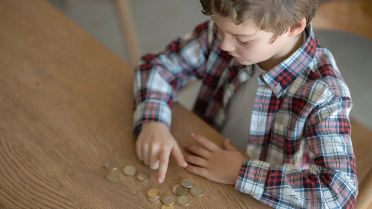A young boy sits at a table counting coins