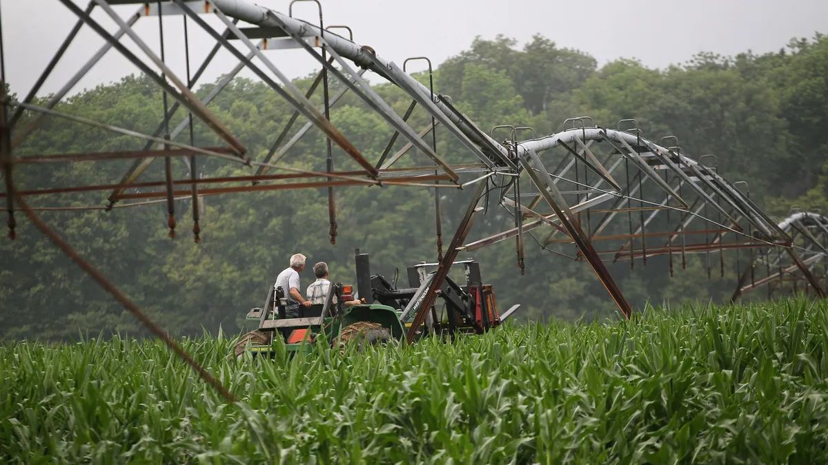 The backs of two men on tractors are seen under a large irrigation system