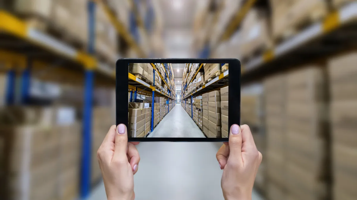 Horizontal color image of female hands holding a digital tablet in a corridor of futuristic distribution warehouse. Ordering