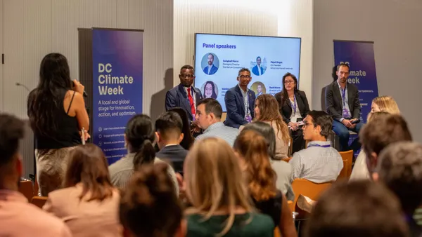 A panel of four speakers looks at a woman asking a question at DC Climate Week