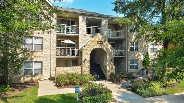 Garden-style apartment with tree and sidewalk in the foreground.
