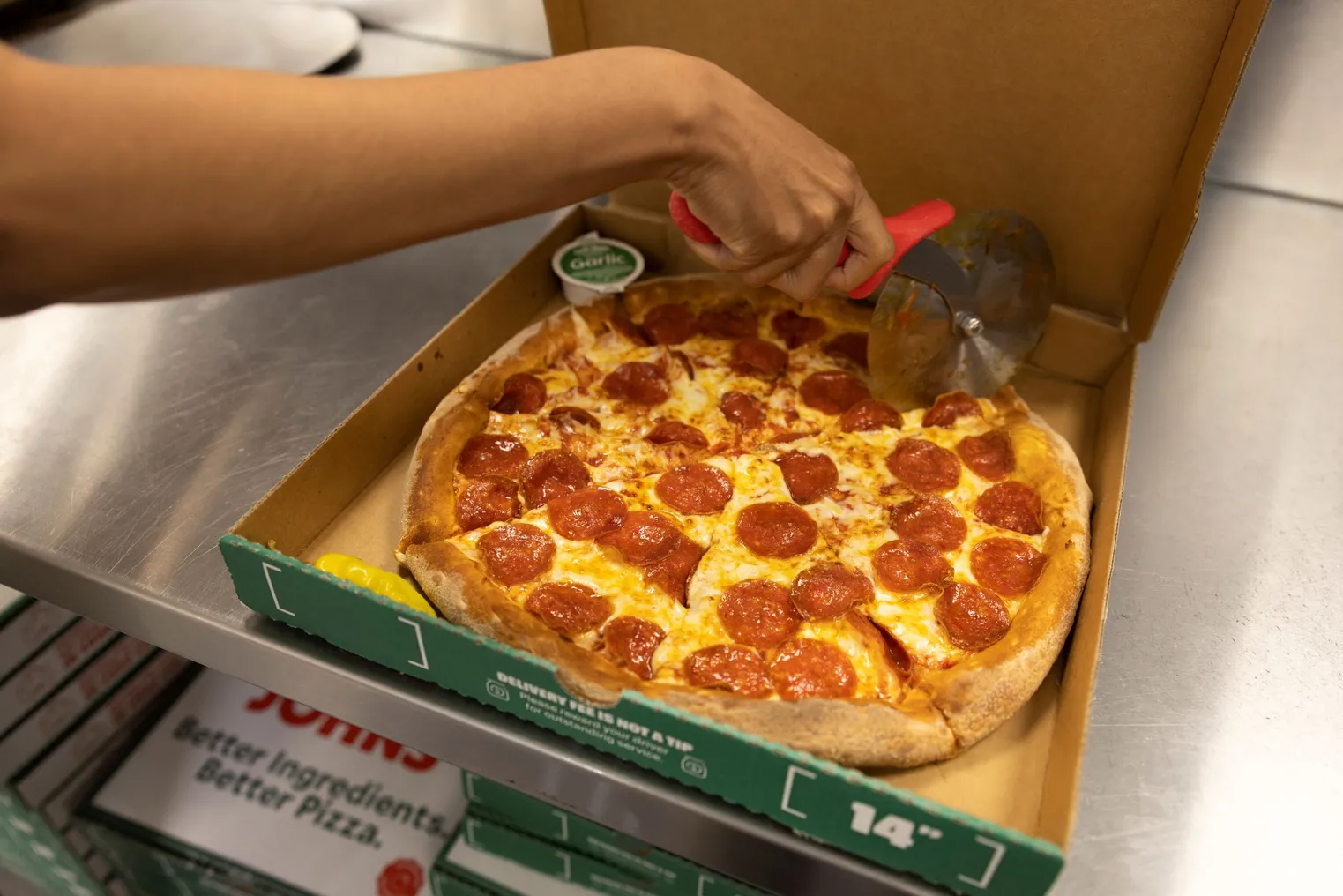 A Papa Johns' employee cuts pizza after preparing it.