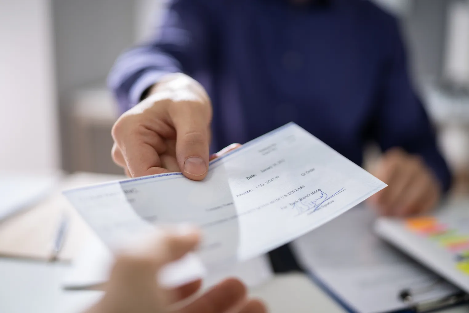 A businessperson hands a colleague a paycheck.