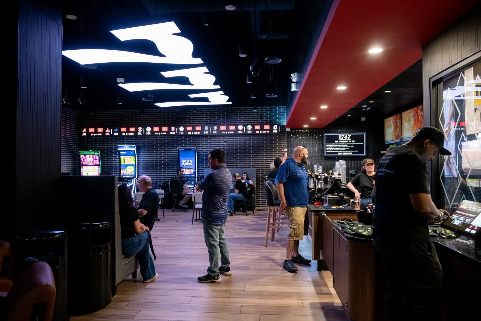 A photo of the interior of a bar area. A large sign saying 777 is on the ceiling and several people are talking or watching TVs.