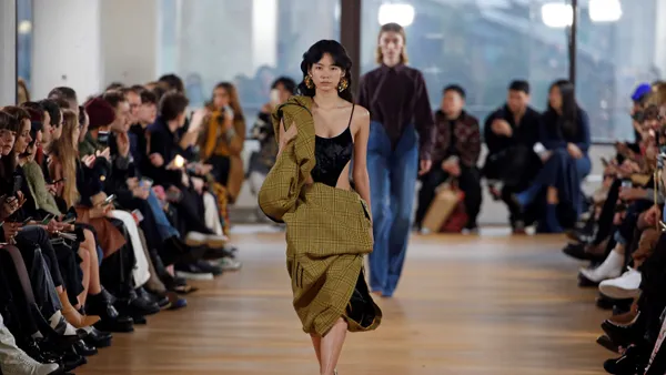 A model walks down the runway during the day as seated crowds watch from the sidelines.