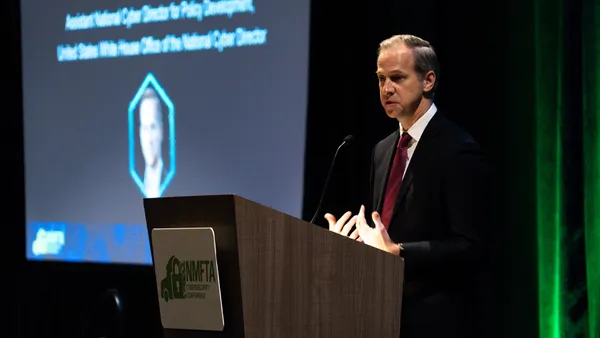 Stephen Viña, with the White House's Office of the National Cyber Director, delivers the conference’s keynote address, standing behind a podium with a computer slide in the background.