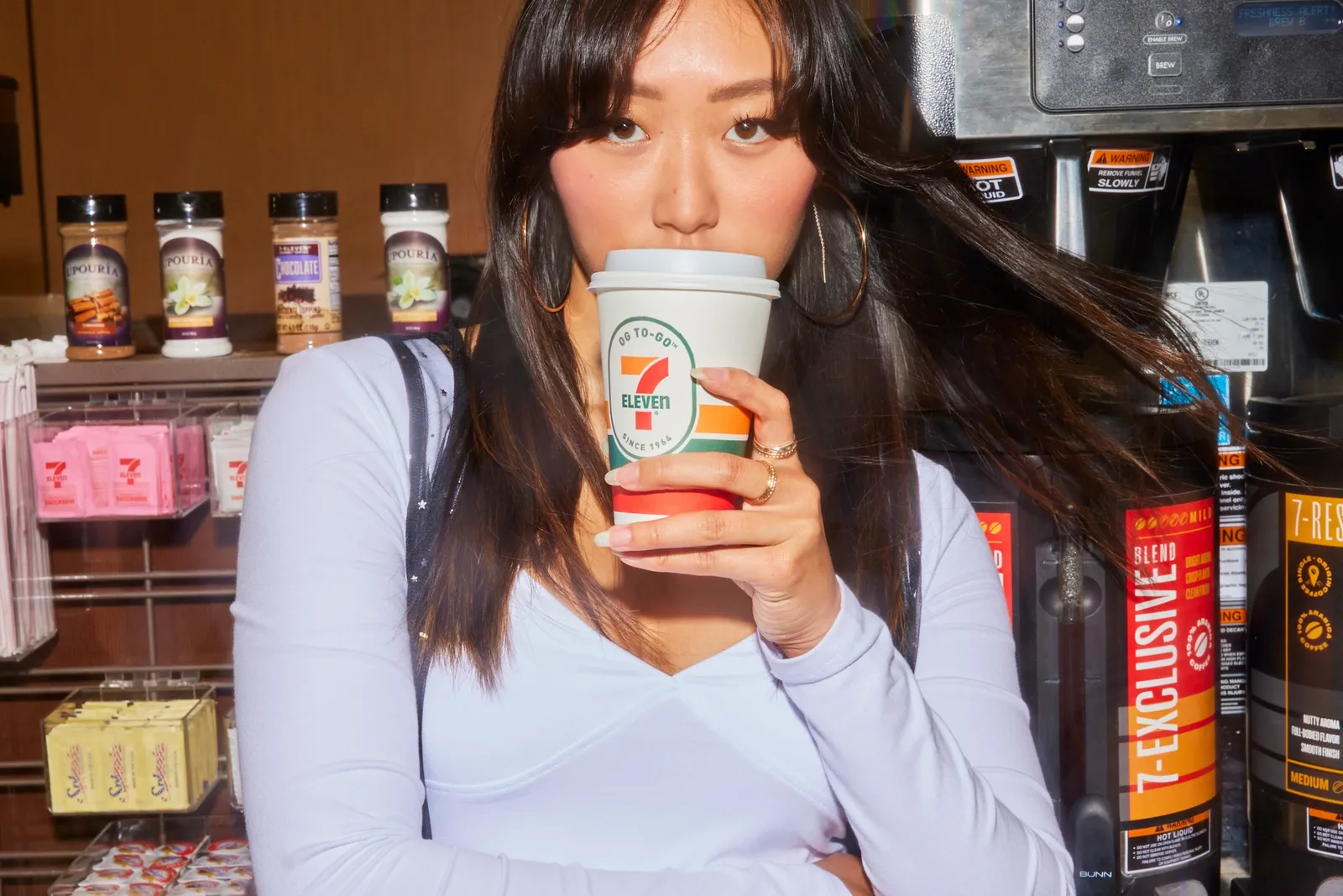 A person drinks from a 7-Eleven-branded hot beverage cup.