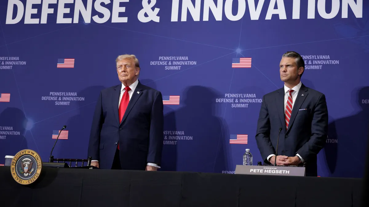 Two people in blue business suits and red ties standing behind a table.
