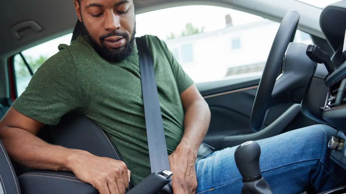 A man seated in the driver's seat of a car buckling his lap and shoulder belt.