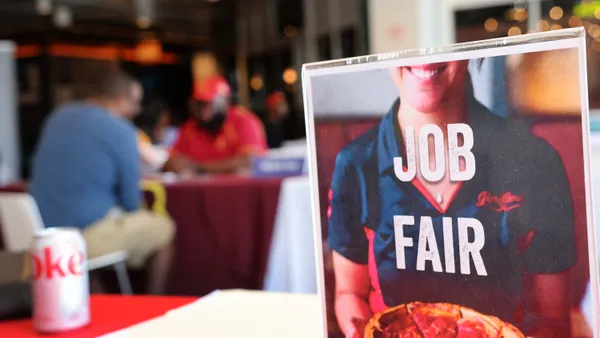 A "job fair" sign is displayed in the foreground and people talk in the background.